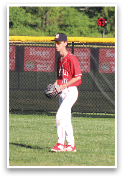 A boy wearing a red shirt and white pants is standing on a baseball field. Description generated by AI