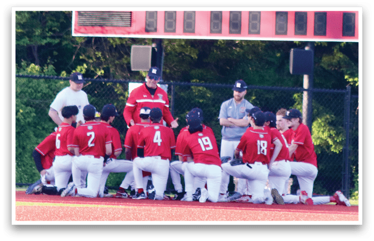 A group of people wearing red shirts are kneeling on a baseball field. Description generated by AI