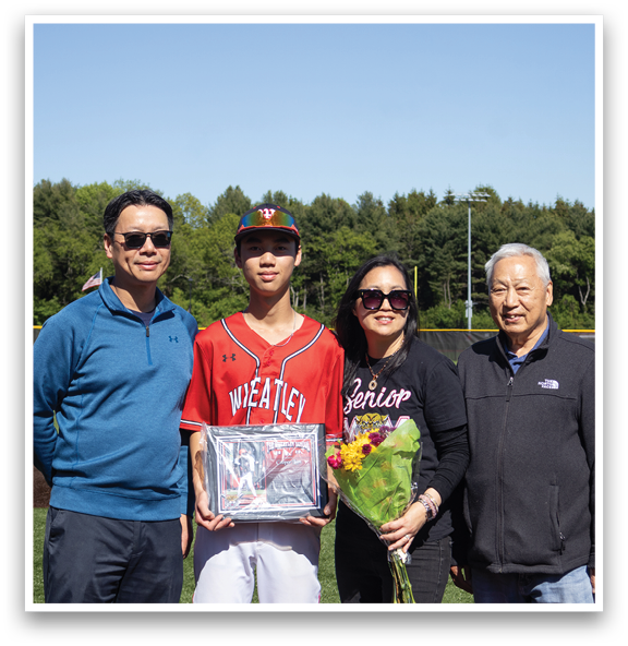 A man holding a baseball trophy with three people behind him. Description generated by AI