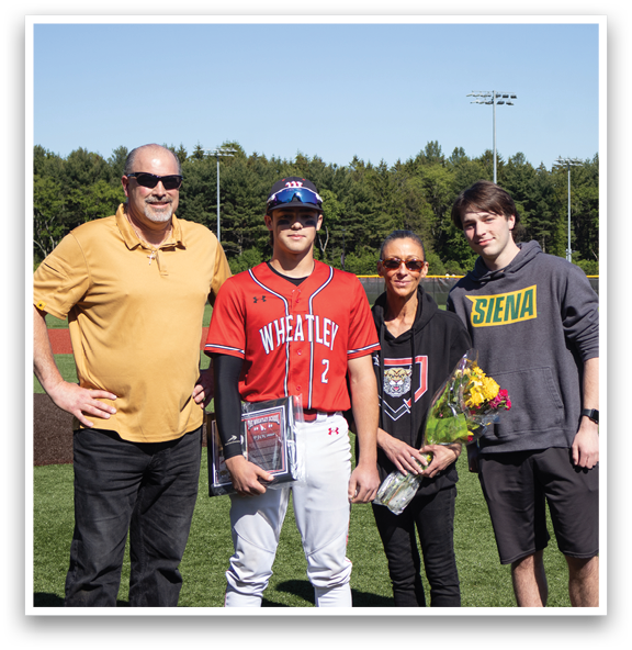 A man in a red jersey stands with his family on a baseball field. Description generated by AI