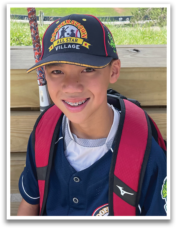 A young boy wearing a blue baseball jersey and a red backpack. Description generated by AI