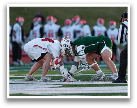 Two men are playing a game of lacrosse, with one player holding a stick and the other holding a ball. They are both wearing helmets for protection. There are several other players on the field, some of whom are wearing green and white uniforms. The scene is set on a grassy field. AI generated content