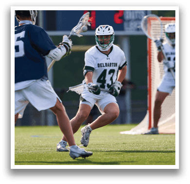 A man in a blue shirt and white shorts is holding a lacrosse stick. Description generated by AI