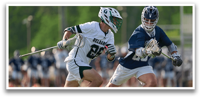 Two men playing lacrosse on a field. Description generated by AI