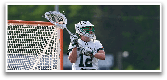 A man wearing a white and green shirt and shorts is holding a lacrosse stick. Description generated by AI