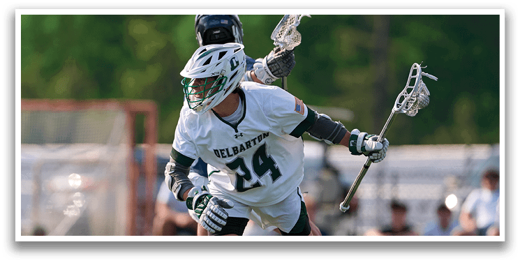 A man wearing a white and green shirt is playing lacrosse. Description generated by AI