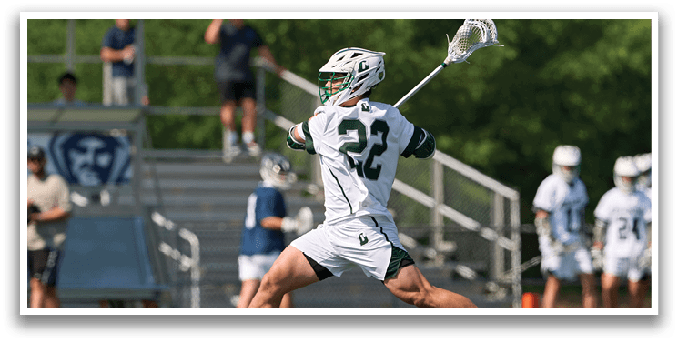 A man wearing a white and green shirt and white shorts is running with a lacrosse stick. Description generated by AI