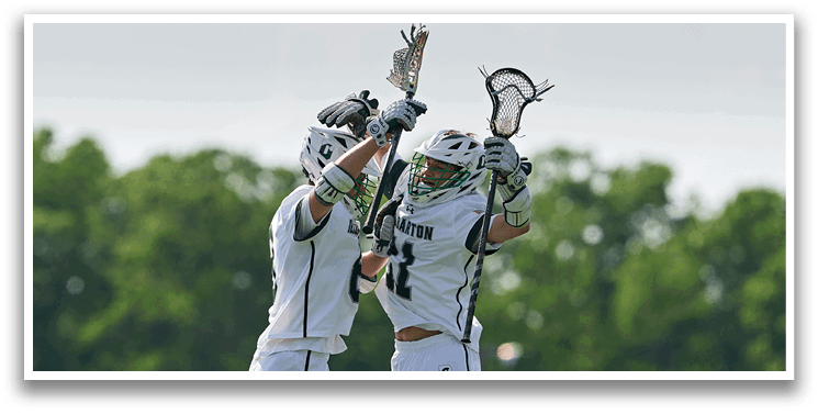 Two men jumping in the air with lacrosse sticks. Description generated by AI