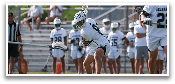 A man in a white shirt and green shorts is running with a lacrosse stick. Description generated by AI