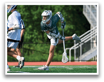 A man in a green shirt and white shorts is holding a lacrosse stick. Description generated by AI