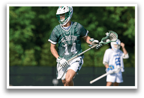 A man wearing a green and white uniform is holding a lacrosse stick. Description generated by AI