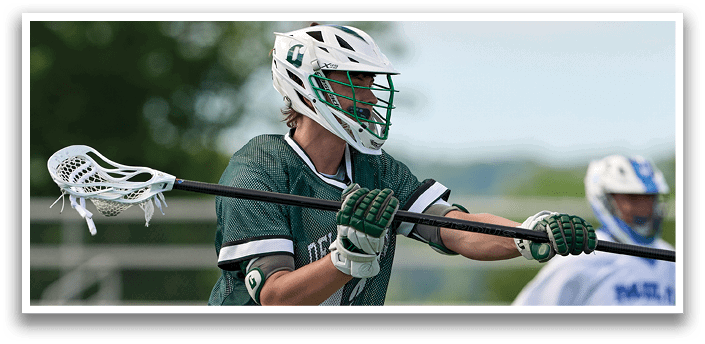 A man wearing a green and white jersey is holding a lacrosse stick. Description generated by AI