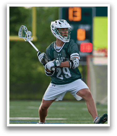 A man wearing a green shirt and white shorts is holding a lacrosse stick. Description generated by AI