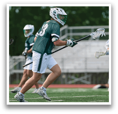 A man wearing a green shirt and white shorts is holding a lacrosse stick. Description generated by AI