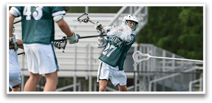 A man in a green shirt is holding a lacrosse stick. Description generated by AI