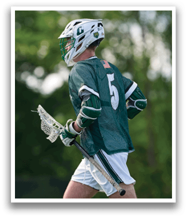 A man wearing a green and white shirt and white shorts is holding a lacrosse stick. Description generated by AI