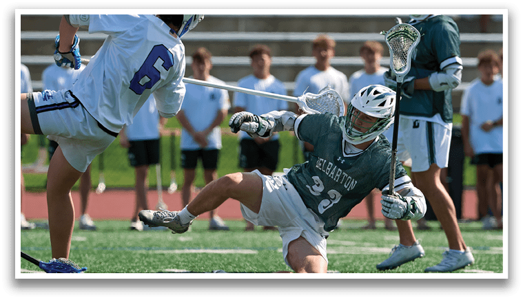 A man is sliding on the ground while another man is holding a lacrosse stick. Description generated by AI