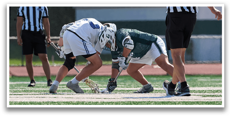 A man wearing a white and green shirt is playing lacrosse. Description generated by AI