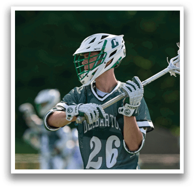 A man wearing a green and white jersey holding a lacrosse stick. Description generated by AI