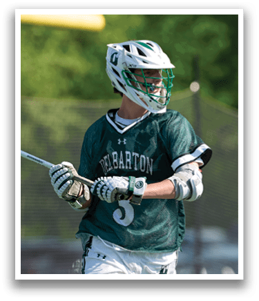 A man wearing a green and white uniform holding a lacrosse stick. Description generated by AI