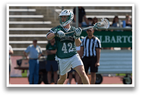 A man in a green shirt and white shorts is holding a lacrosse stick. Description generated by AI