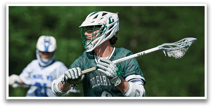A man wearing a green and white shirt holding a lacrosse stick. Description generated by AI