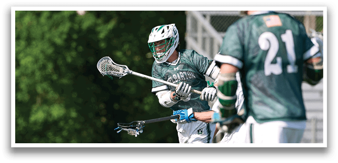 A man in a green shirt is holding a lacrosse stick. Description generated by AI