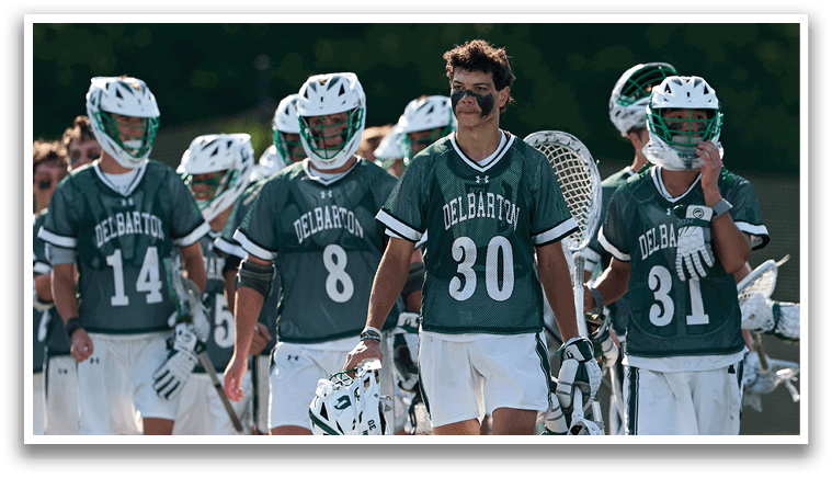 A man in a green shirt and white shorts is running with a lacrosse stick. Description generated by AI