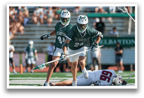 A man wearing a green and white uniform is holding a lacrosse stick. Description generated by AI