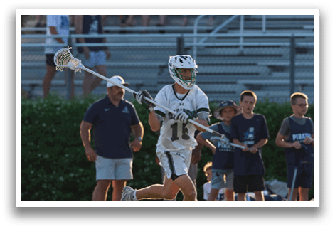 A man in a green and white uniform is holding a stick and running on a field. Description generated by AI
