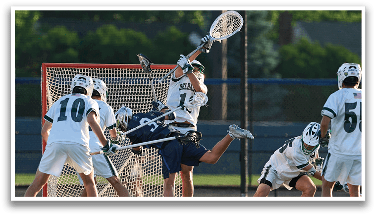 A man wearing a green shirt and white shorts holding a lacrosse stick. Description generated by AI
