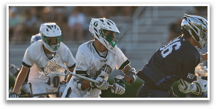 A man wearing a white and green shirt is playing lacrosse. Description generated by AI