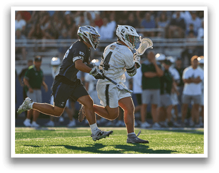 A man wearing a green and white shirt and white pants holding a lacrosse stick. Description generated by AI
