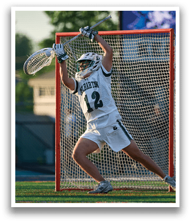 A man running on a field with a lacrosse stick. Description generated by AI