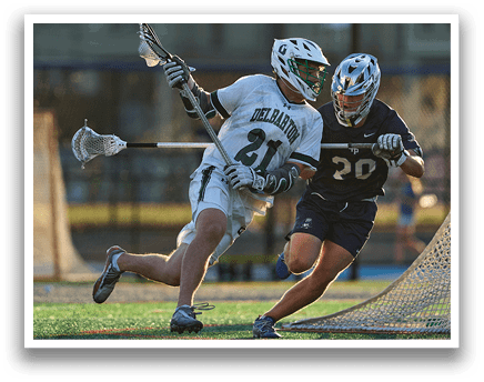 A man in a green shirt and white shorts is holding a lacrosse stick. Description generated by AI