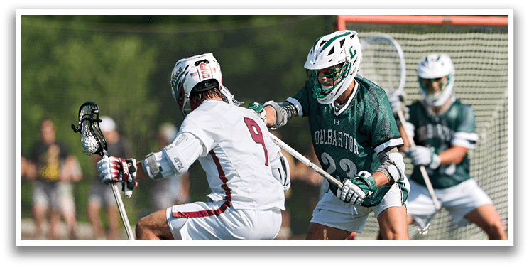 A man wearing a white and green shirt is playing lacrosse. Description generated by AI