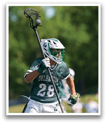 A man wearing a green and white uniform holding a lacrosse stick. Description generated by AI