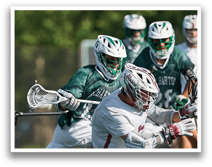 A man wearing a green and white shirt and white pants holding a lacrosse stick. Description generated by AI