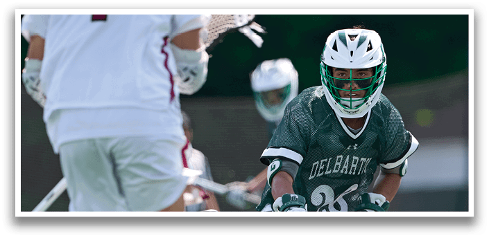 A man in a green shirt and white shorts is running with a lacrosse stick. Description generated by AI