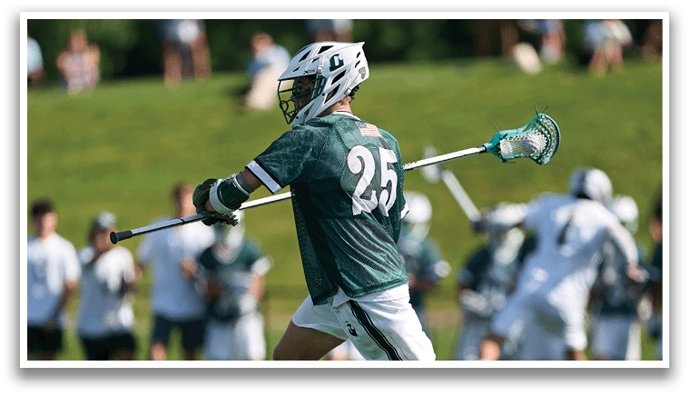 A man wearing a green shirt and white shorts holding a lacrosse stick. Description generated by AI
