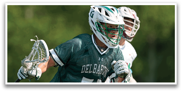 A man wearing a green and white shirt holding a lacrosse stick. Description generated by AI