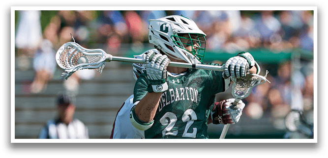 A man in a green shirt is holding a lacrosse stick. Description generated by AI