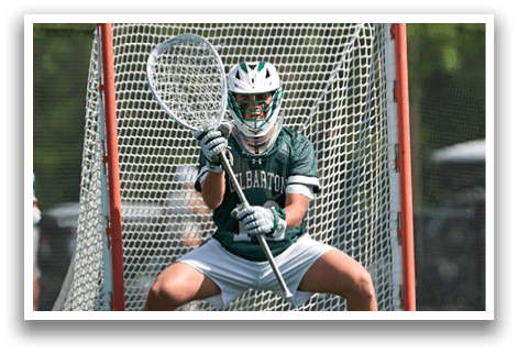 A man in a green and white uniform is holding a stick and running on a field. Description generated by AI