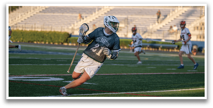 A man in a green shirt is running with a lacrosse stick. Description generated by AI