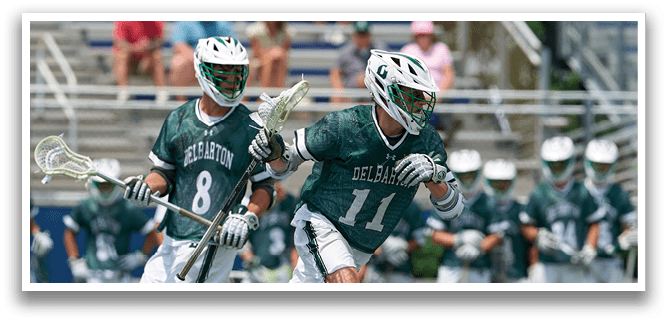 A man in a green shirt is holding a lacrosse stick. Description generated by AI