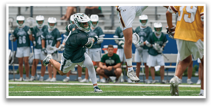 A man wearing a white and green shirt is playing lacrosse. Description generated by AI