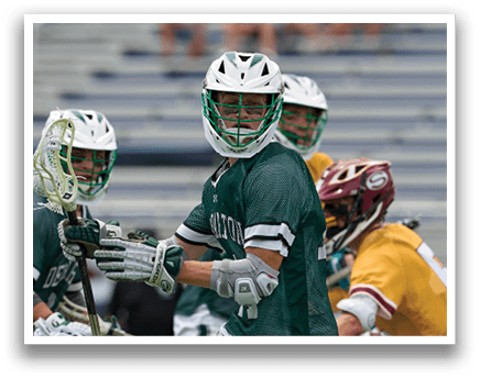 A man in a green shirt and white shorts is holding a lacrosse stick. Description generated by AI