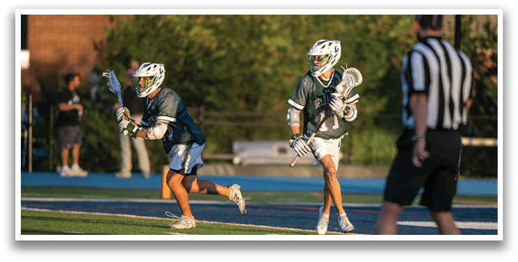A man wearing a white and green shirt is playing lacrosse. Description generated by AI