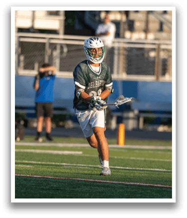 A man wearing a green and white uniform holding a lacrosse stick. Description generated by AI