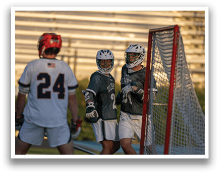 A man wearing a green and white shirt and white pants holding a lacrosse stick. Description generated by AI